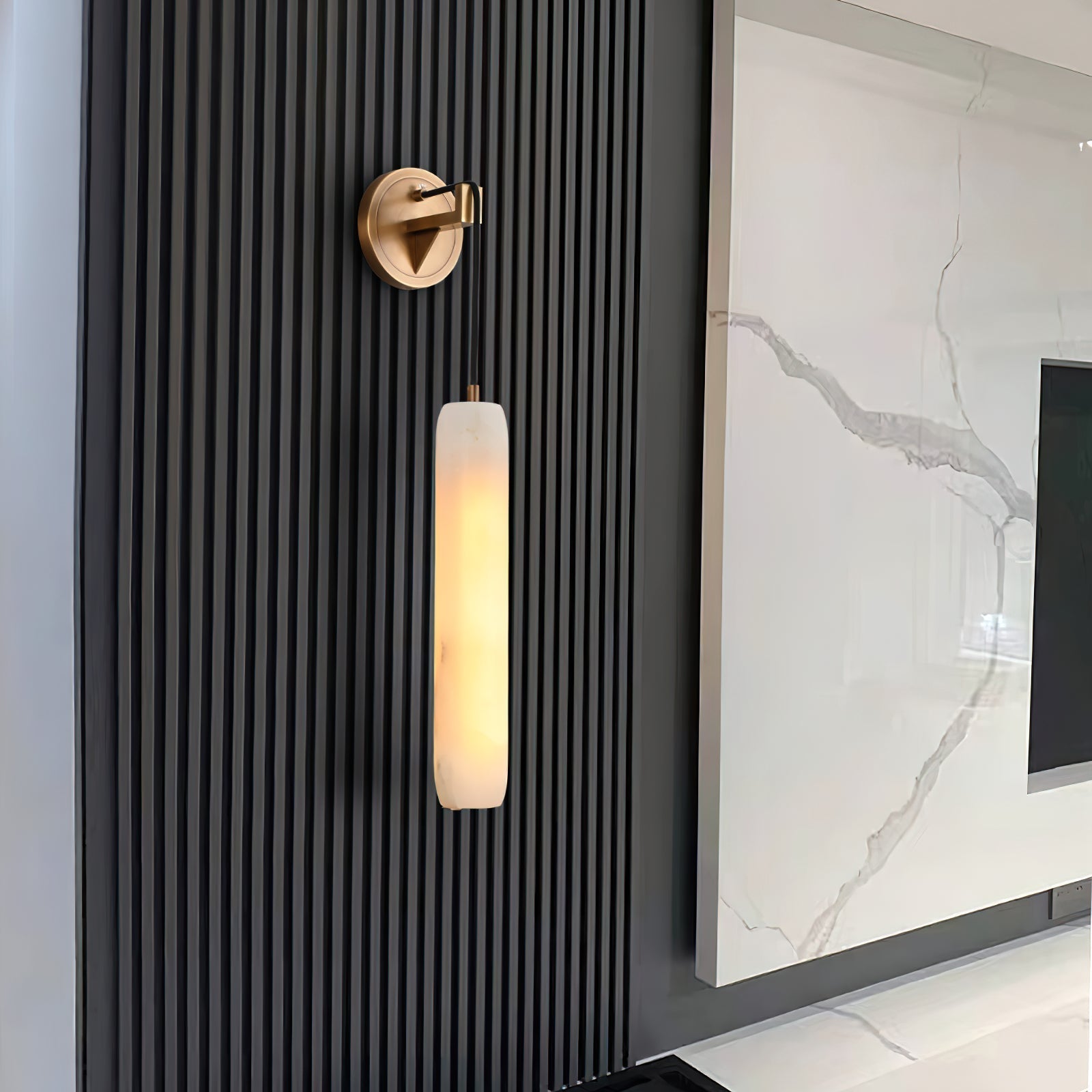 The Clérachic sconce on a black fluted timber wall, its warm column set against a veined marble media panel.