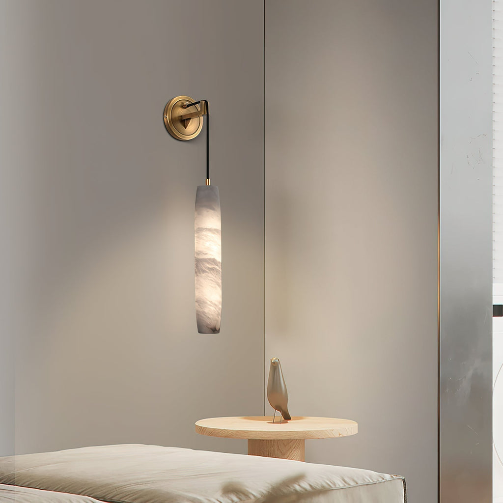 The Clérachic sconce beside a bed, its light falling over a small round table holding a carved bird ornament.