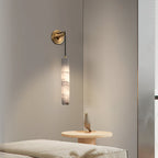 The Clérachic sconce beside a bed, its light falling over a small round table holding a carved bird ornament.