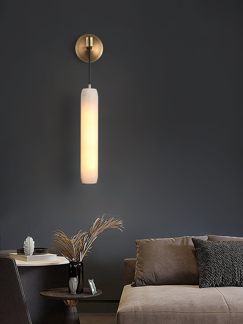 The Clérachic sconce against a charcoal living-room wall above a side table of dried grasses and a low sofa.