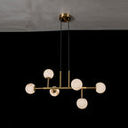 Clérachic Alabaster Globe Chandelier in its six-light frame, globes lit amber against a dark dining wall.