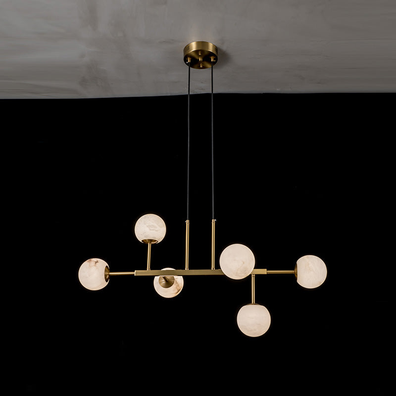 Clérachic Alabaster Globe Chandelier in its six-light frame, globes lit amber against a dark dining wall.