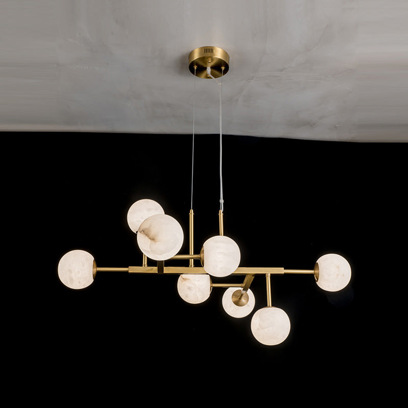 Clérachic Alabaster Globe Chandelier with nine lit globes branching along its brass bar, seen from below in a dark room.