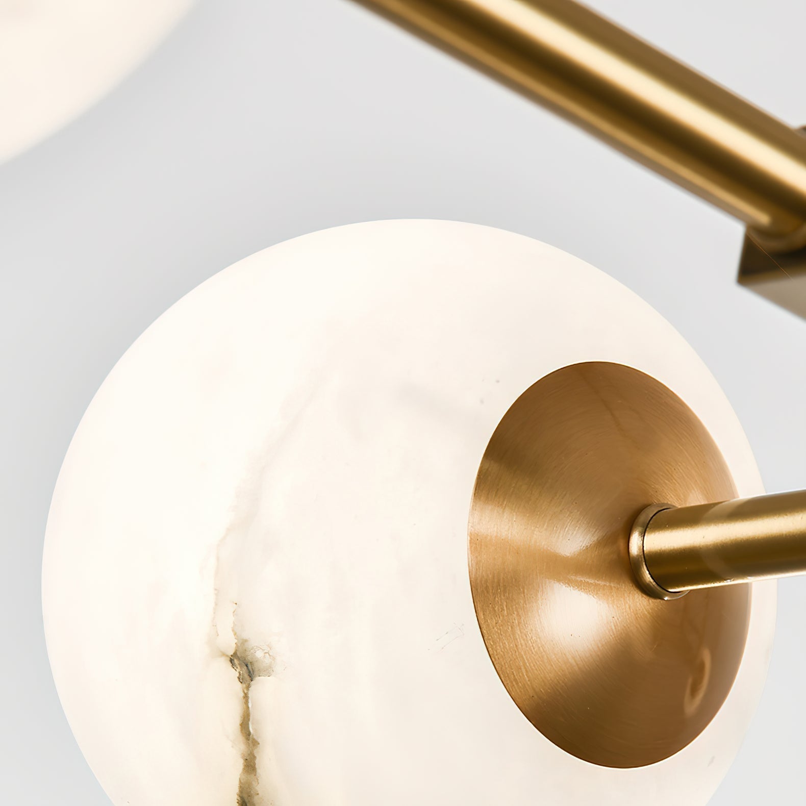 Detail of a brass cup seated in an alabaster sphere on the Clérachic Alabaster Globe Chandelier, arm joining from the right.