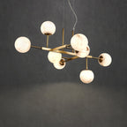 Clérachic Alabaster Globe Chandelier lit against a grey concrete wall, nine stone globes staggered across the brass frame.