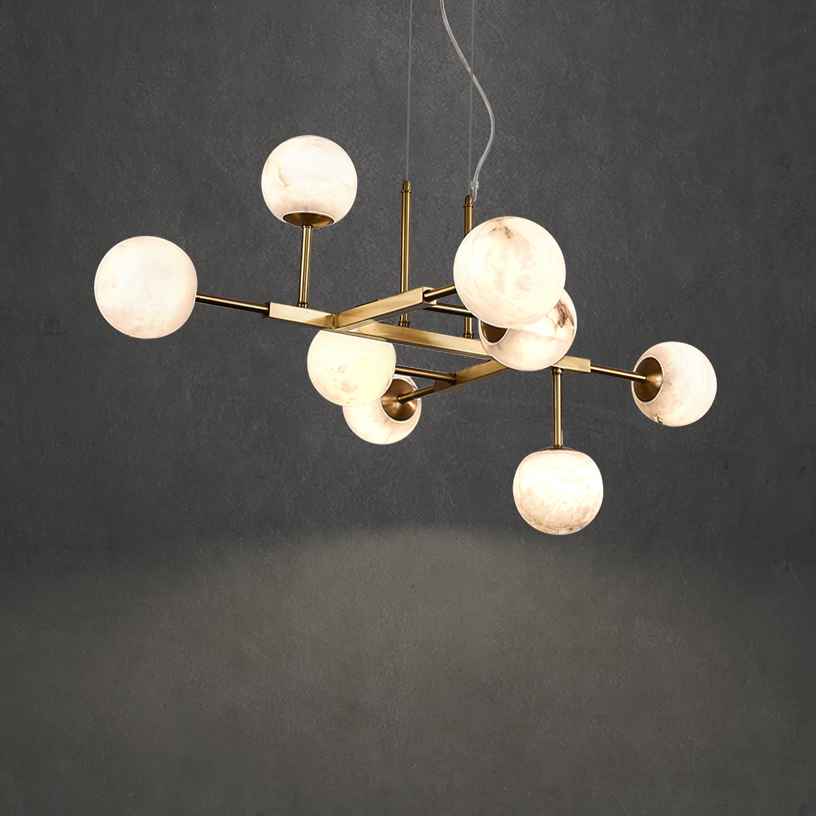 Clérachic Alabaster Globe Chandelier lit against a grey concrete wall, nine stone globes staggered across the brass frame.