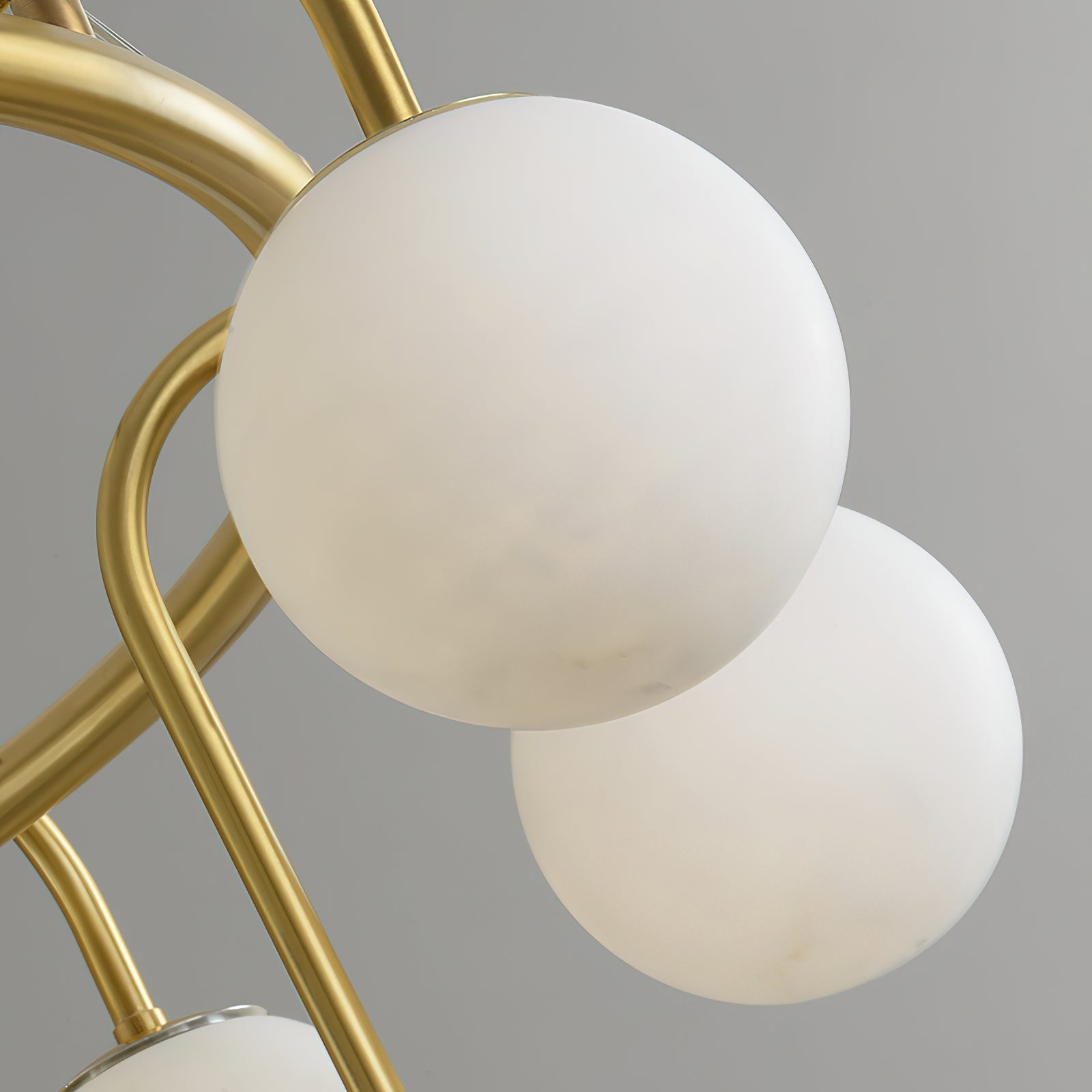 Close-up of the Clérachic Alabaster Globe Chandelier, two stone globes meeting where a curved brass arm crosses the ring.