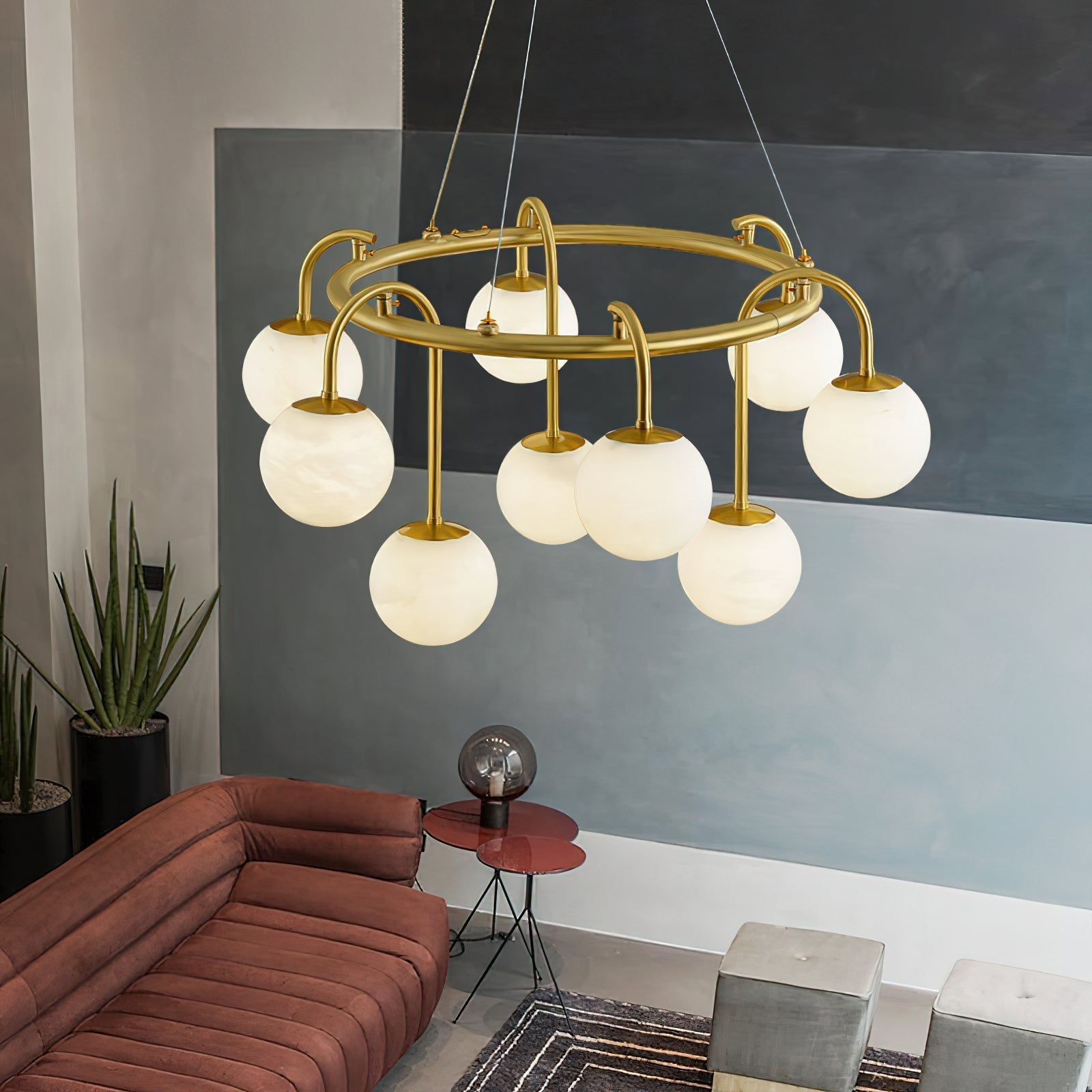 The Clérachic Alabaster Globe Chandelier unlit in a painted concrete lounge, nine stone globes above a rust sofa and potted plants.