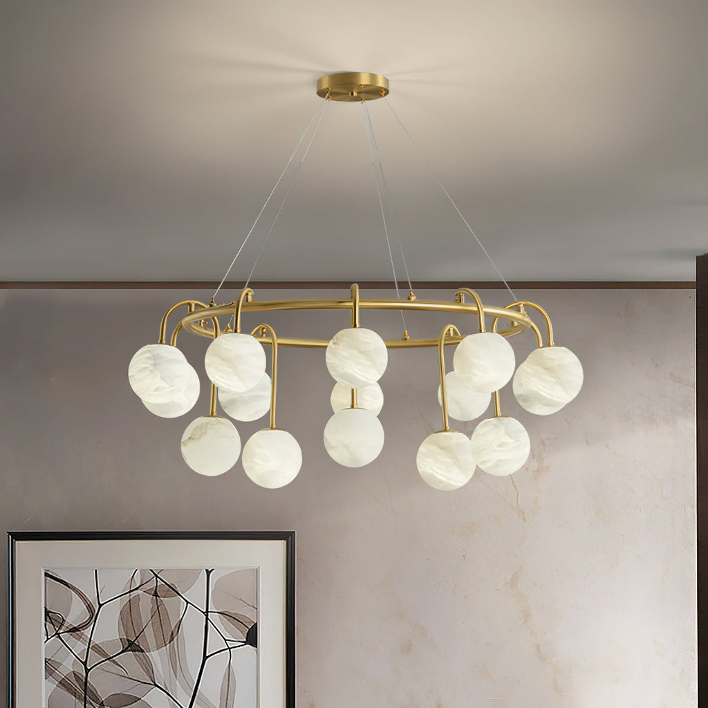 The Clérachic Alabaster Globe Chandelier in its fifteen-light width, lit above framed artwork on a warm travertine wall.