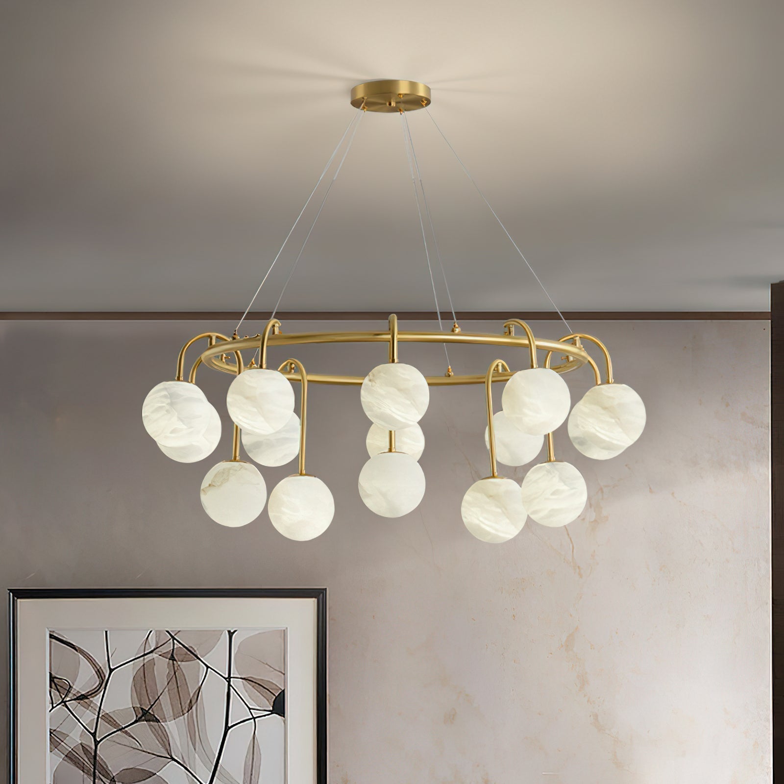 The Clérachic Alabaster Globe Chandelier in its fifteen-light width, lit above framed artwork on a warm travertine wall.