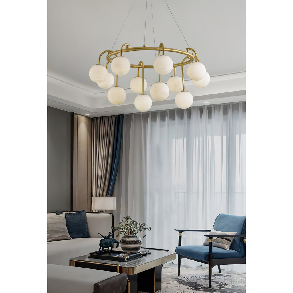 Clérachic Alabaster Globe Chandelier hanging in a bright living room by sheer curtains, above a blue armchair and marble table.