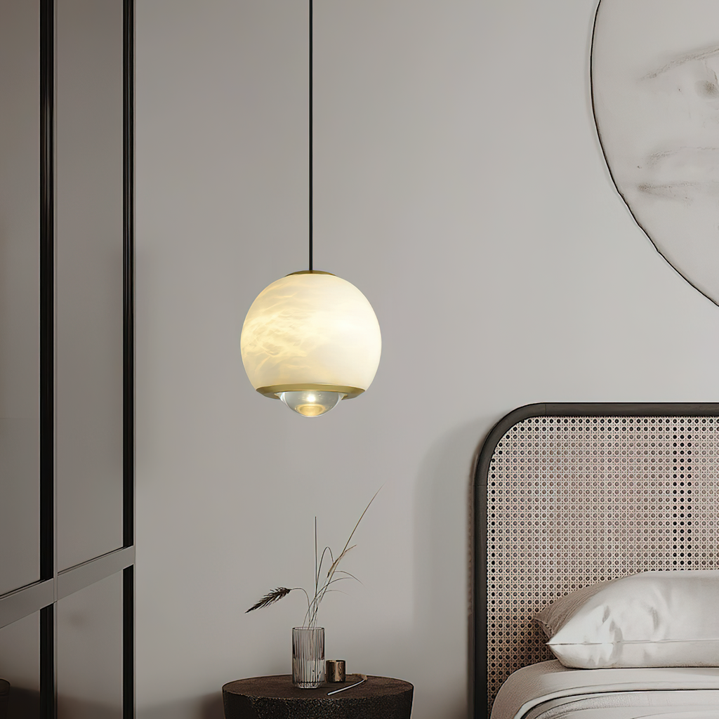 Clérachic Alabaster Globe Pendant Light glowing honey-cream beside a caned bed, its brass band and lens aimed at the side table below.