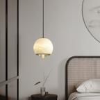 Clérachic Alabaster Globe Pendant Light glowing honey-cream beside a caned bed, its brass band and lens aimed at the side table below.