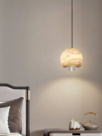 A Clérachic Alabaster Globe Pendant Light beside a bed, casting a soft cone of warm light down the wall over a teapot and stone tray.