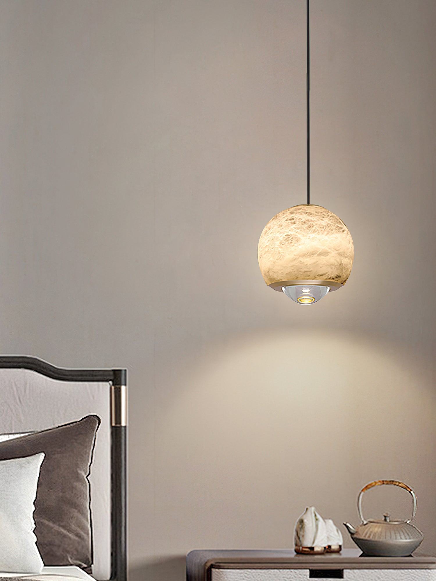 A Clérachic Alabaster Globe Pendant Light beside a bed, casting a soft cone of warm light down the wall over a teapot and stone tray.