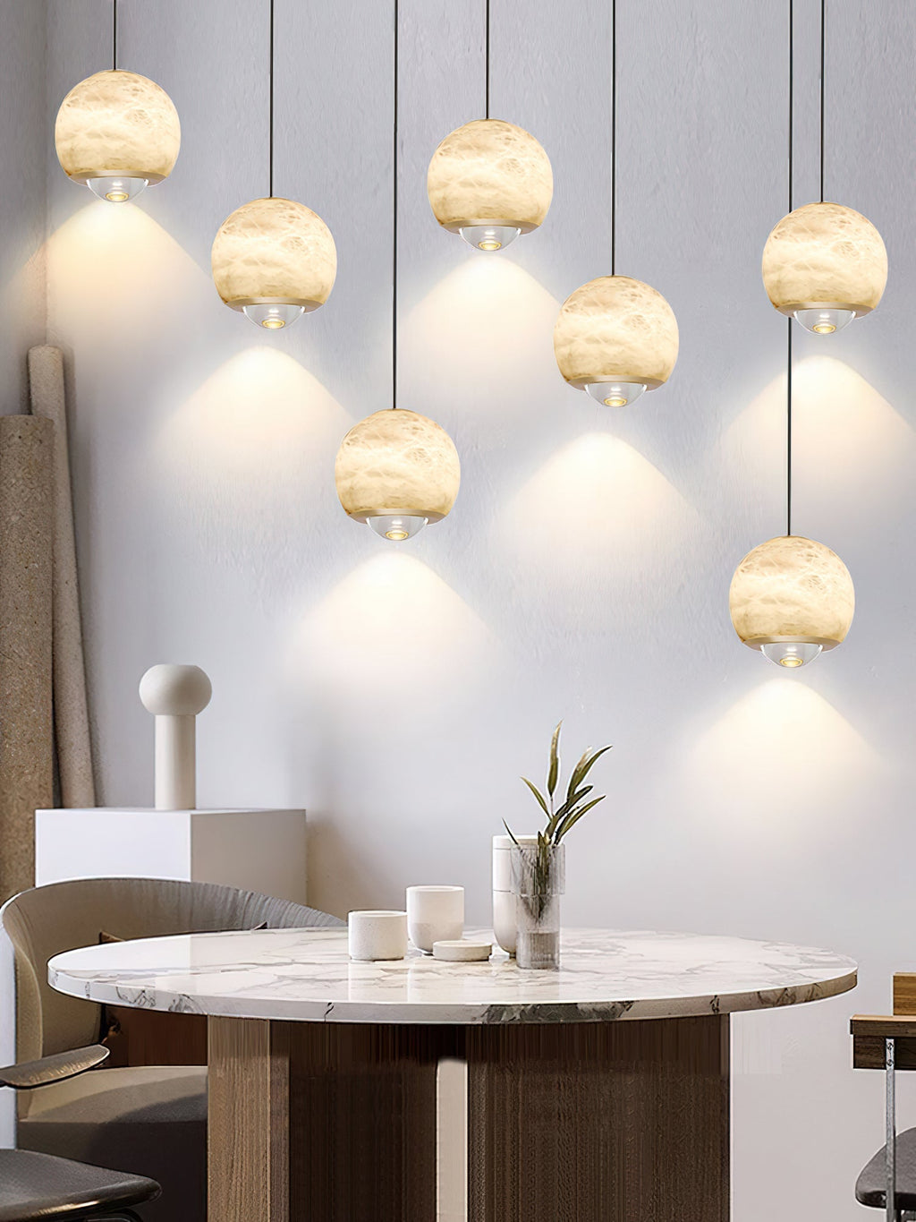 Seven Clérachic Alabaster Globe Pendant Lights staggered above a marble table, each lens dropping its own cone of light onto the wall.
