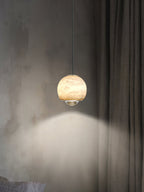 Clérachic Alabaster Globe Pendant Light against a raw plaster wall and linen curtain, the stone lit while the lens washes the wall beneath it.