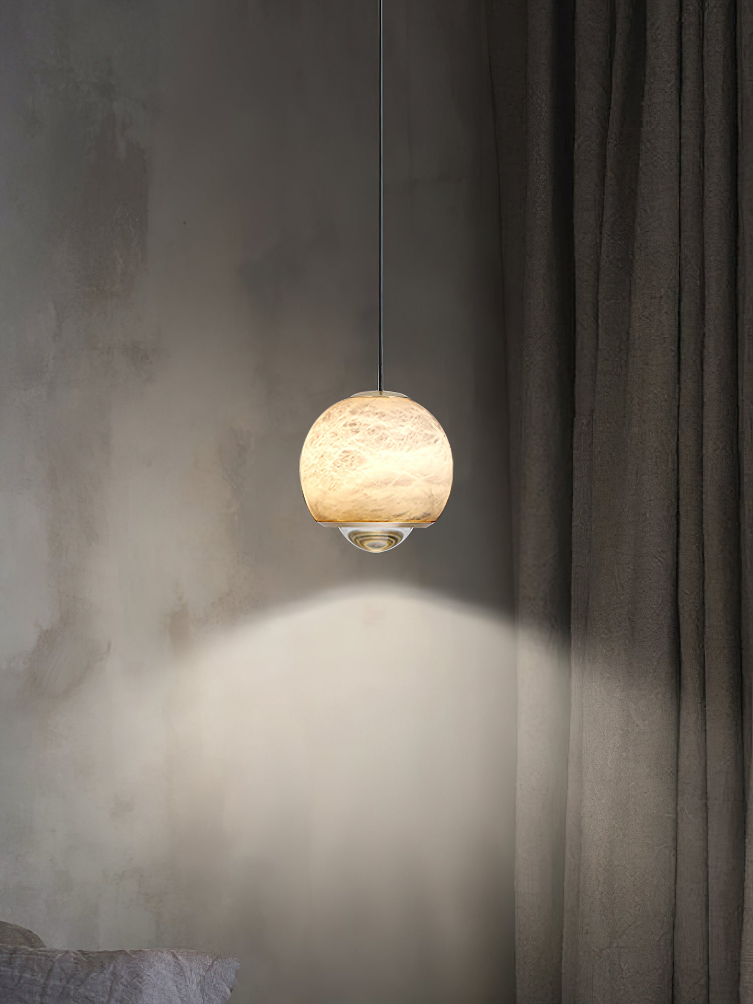 Clérachic Alabaster Globe Pendant Light against a raw plaster wall and linen curtain, the stone lit while the lens washes the wall beneath it.