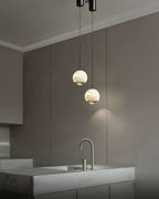Clérachic Alabaster Globe Pendant Lights hung as a pair over a marble kitchen island, lighting the tap and counter from a high ceiling.