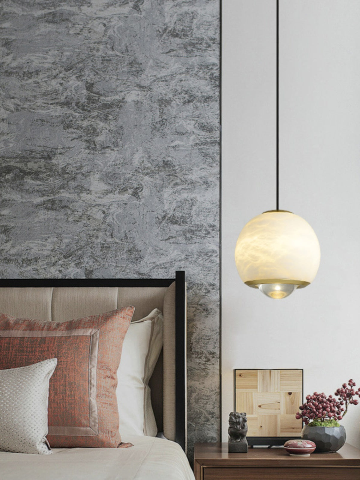 Clérachic Alabaster Globe Pendant Light lit beside a stone-clad bedroom wall, brass collar and base ring catching light above a nightstand.