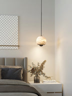 Clérachic Alabaster Globe Pendant Light over a white bedside table of dried eucalyptus and books, spilling a warm pool onto the wall.