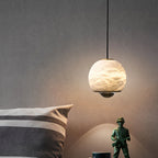 Clérachic Alabaster Globe Pendant Light lit close to a grey wall, the stone reading warm above a striped pillow and a toy figure.