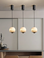 Three Clérachic Alabaster Globe Pendant Lights in a row from black ceiling canopies, hung over a counter set with a teapot and dried stems.