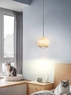 Clérachic Alabaster Globe Pendant Light in a blue-grey bedroom with two cats, lighting a wooden nightstand, clock and small bottle.