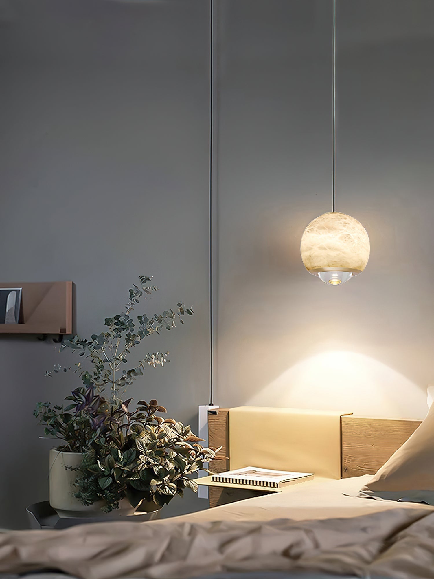 Clérachic Alabaster Globe Pendant Light on a long cord in a dark bedroom, its beam falling across a timber shelf and potted eucalyptus.