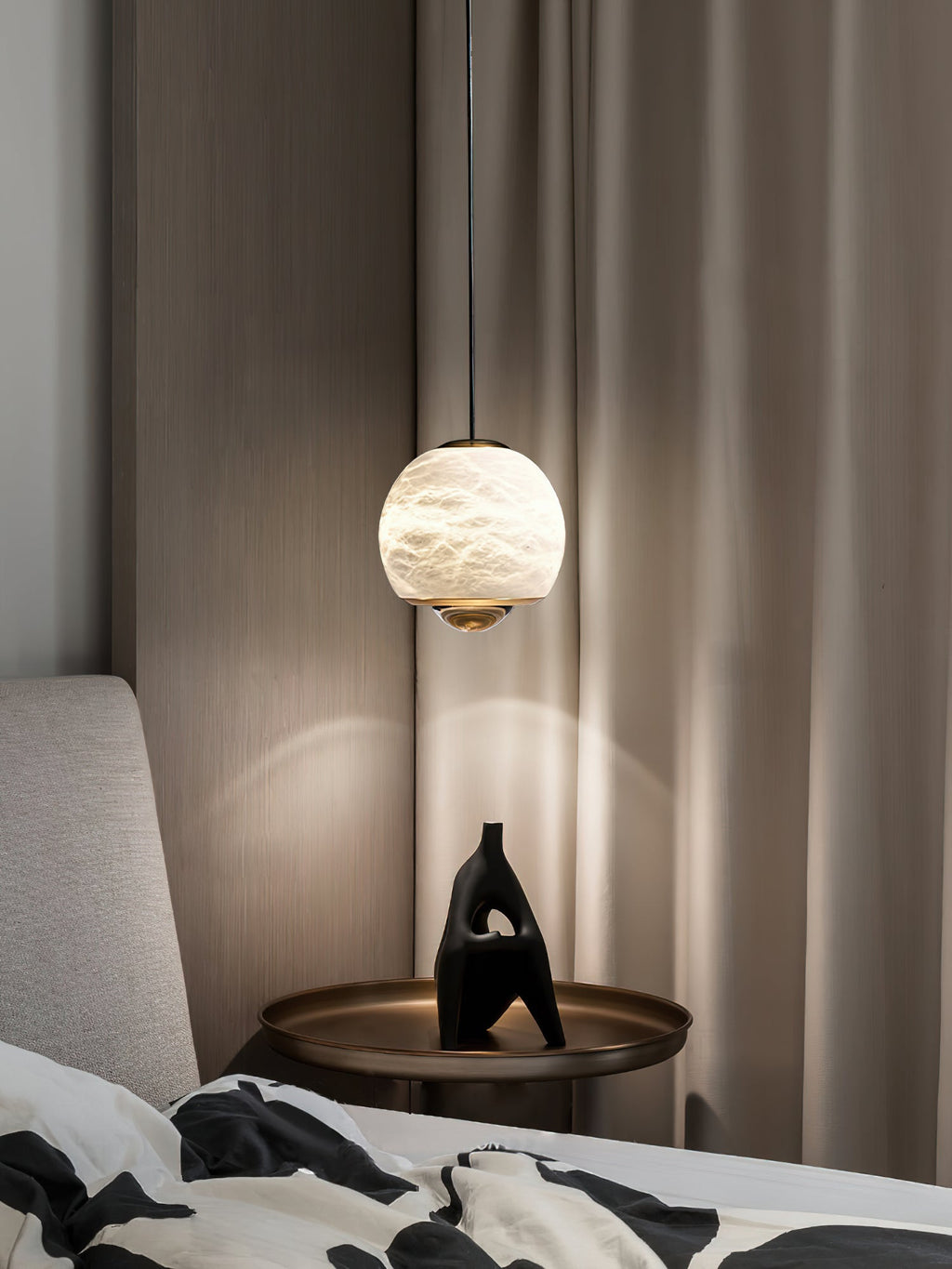Clérachic Alabaster Globe Pendant Light lighting a bronze bedside tray and black sculpture, with drapery and fluted panelling behind.