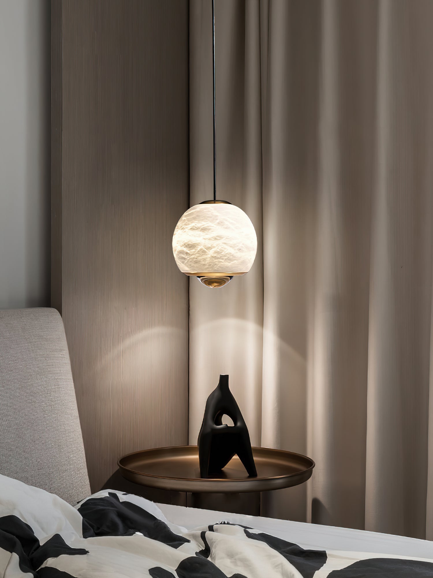 Clérachic Alabaster Globe Pendant Light lighting a bronze bedside tray and black sculpture, with drapery and fluted panelling behind.