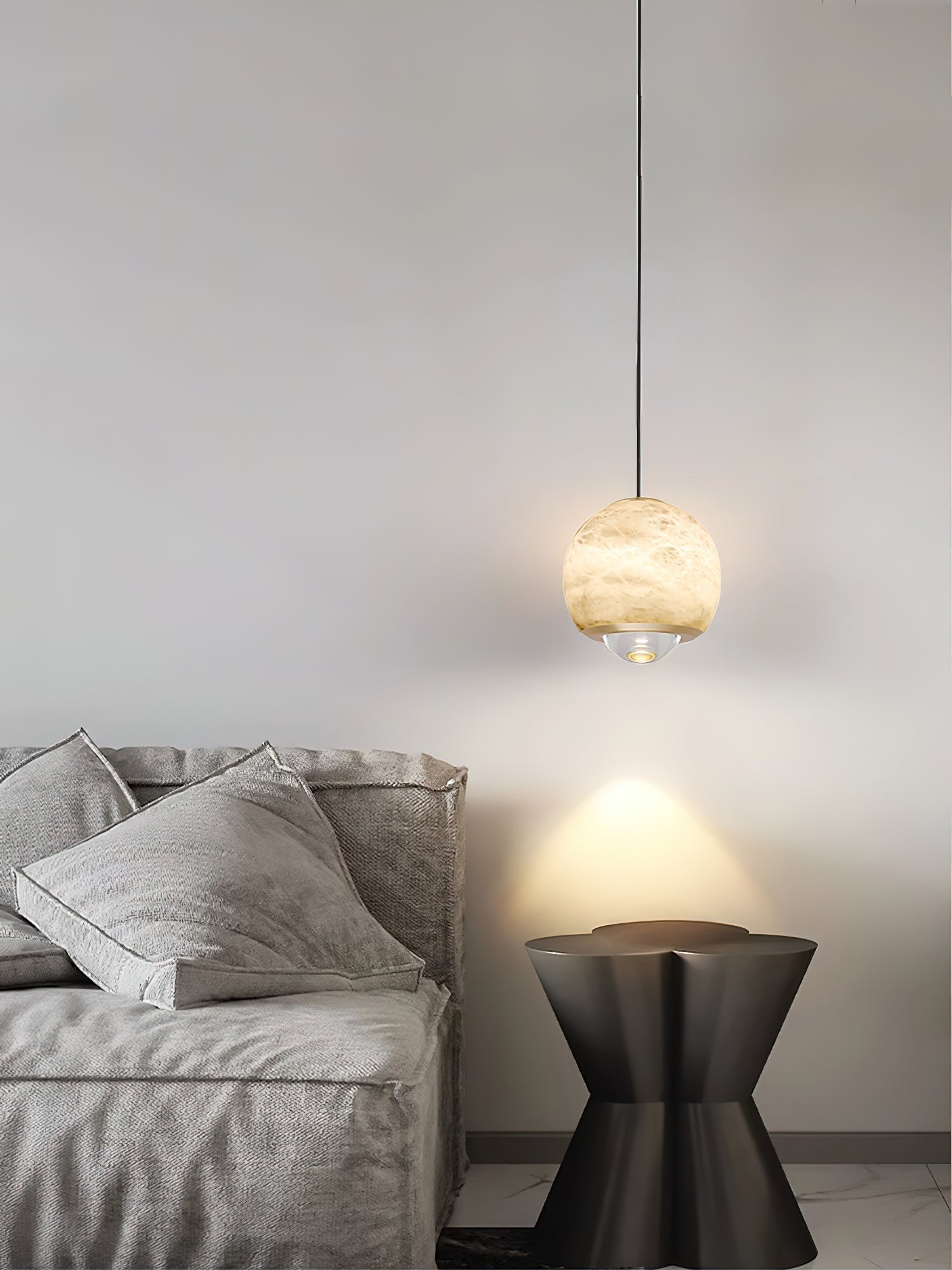 Clérachic Alabaster Globe Pendant Light dropping on a long cord beside a grey upholstered bed, lighting a black hourglass side table.