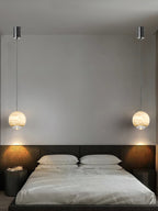 A matched pair of Clérachic Alabaster Globe Pendant Lights hung either side of a bed, each on a long cord from a black ceiling canopy.