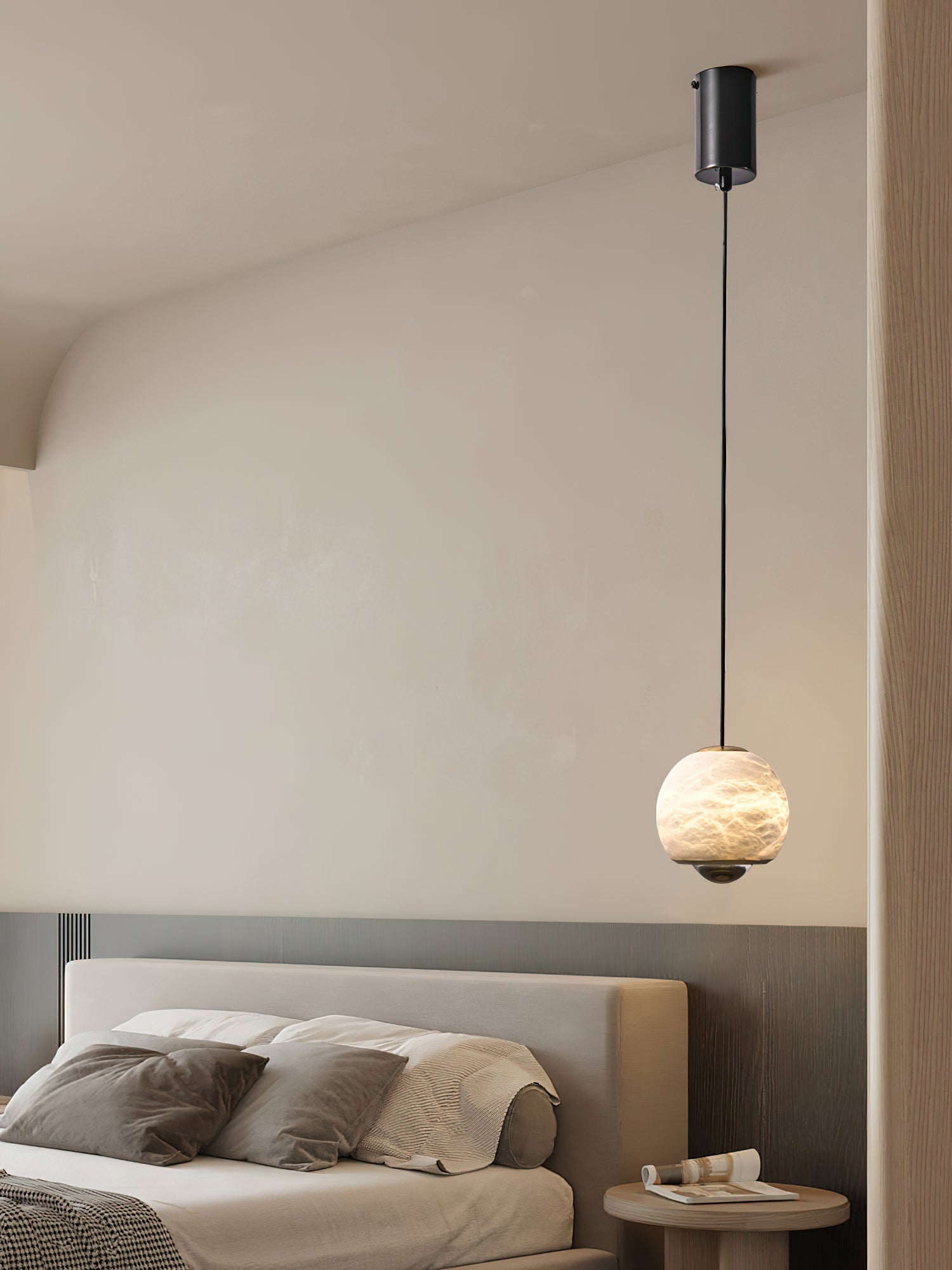 Clérachic Alabaster Globe Pendant Light on a long drop from a black canopy, glowing low beside a bed in a soft cream bedroom.