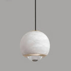 Detail of the Clérachic Alabaster Globe Pendant Light unlit on grey, chalk-white stone set between two brass rings above the clear lens.