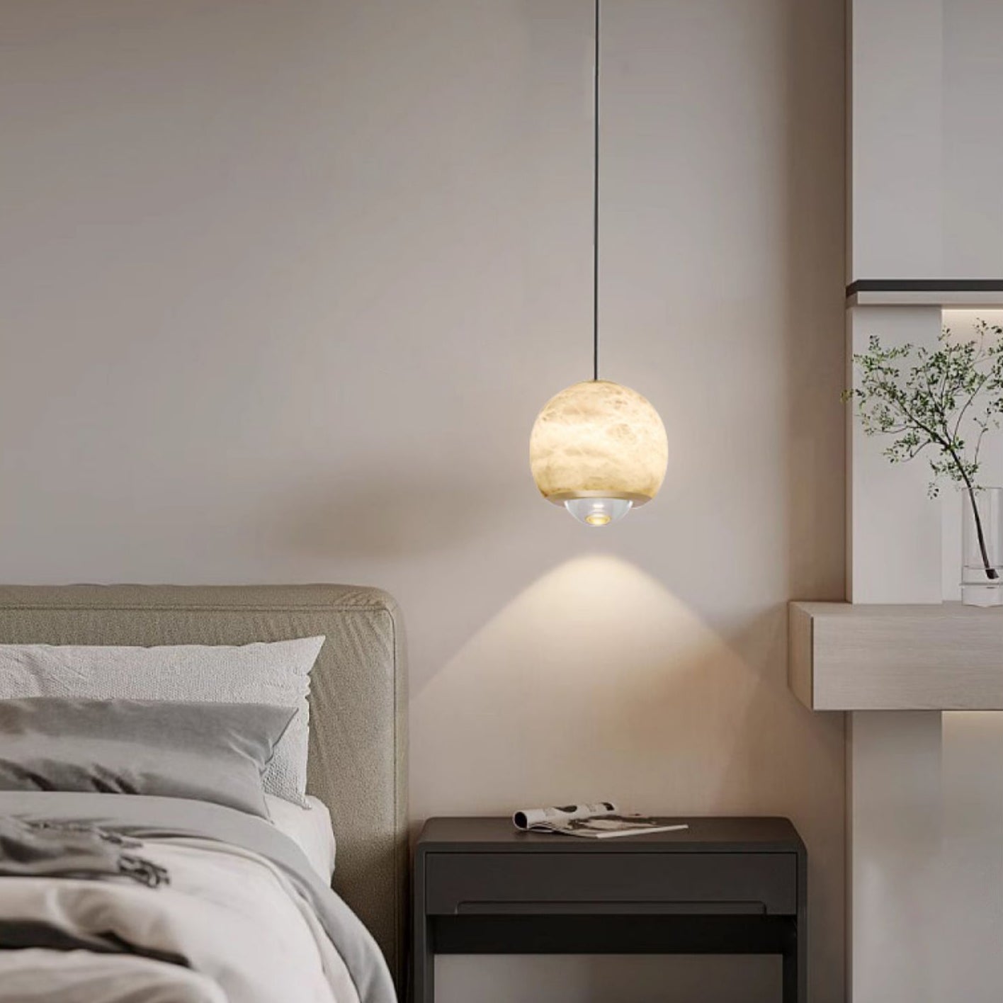 Clérachic Alabaster Globe Pendant Light beside a beige bed, its downward beam drawing a clean cone of light on the wall above a black nightstand.