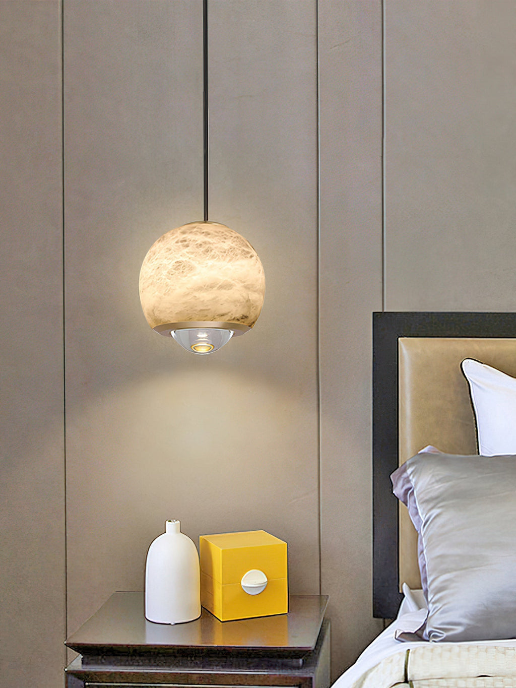 Clérachic Alabaster Globe Pendant Light against padded wall panels, lighting a metal nightstand with a white vase and a yellow box.