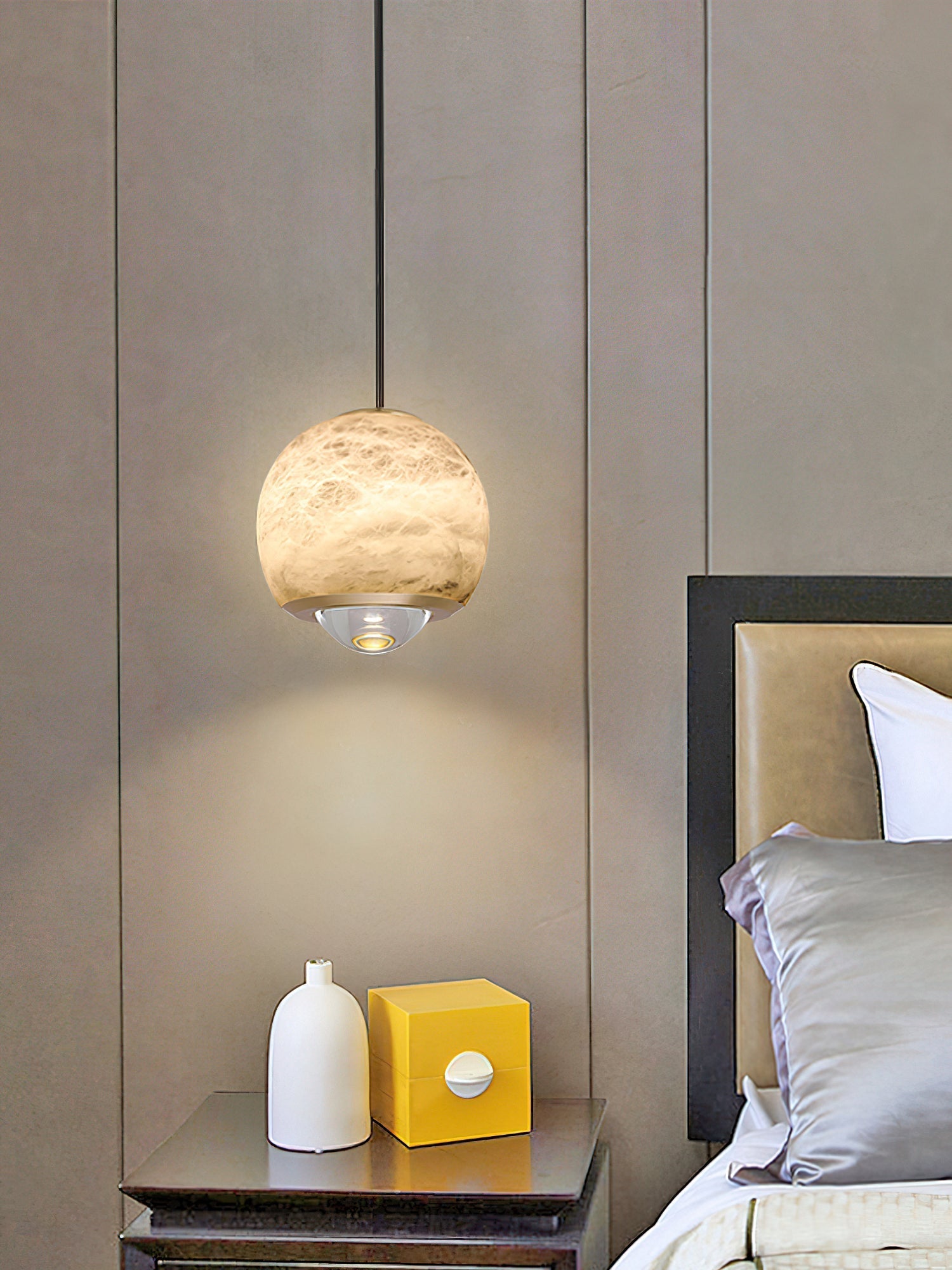 Clérachic Alabaster Globe Pendant Light against padded wall panels, lighting a metal nightstand with a white vase and a yellow box.