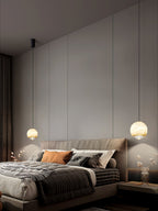 Two Clérachic Alabaster Globe Pendant Lights at different drops flanking a bed in a dim panelled bedroom, each pooling light on the wall.
