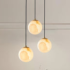 Clérachic Alabaster Globe Pendant Light in its three-globe cluster, brass collars catching the light above a moulded wall.