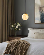 Clérachic Alabaster Globe Pendant Light lit above a bedside table of white roses, glowing honey against a deep grey bedroom wall.