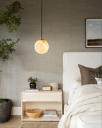 A single Clérachic Alabaster Globe Pendant Light beside a pale bedside chest, its warm stone reading against a grasscloth wall.