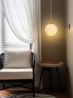 Clérachic Alabaster Globe Pendant Light on a white cord over a round side table, lighting a rattan reading chair by the window.