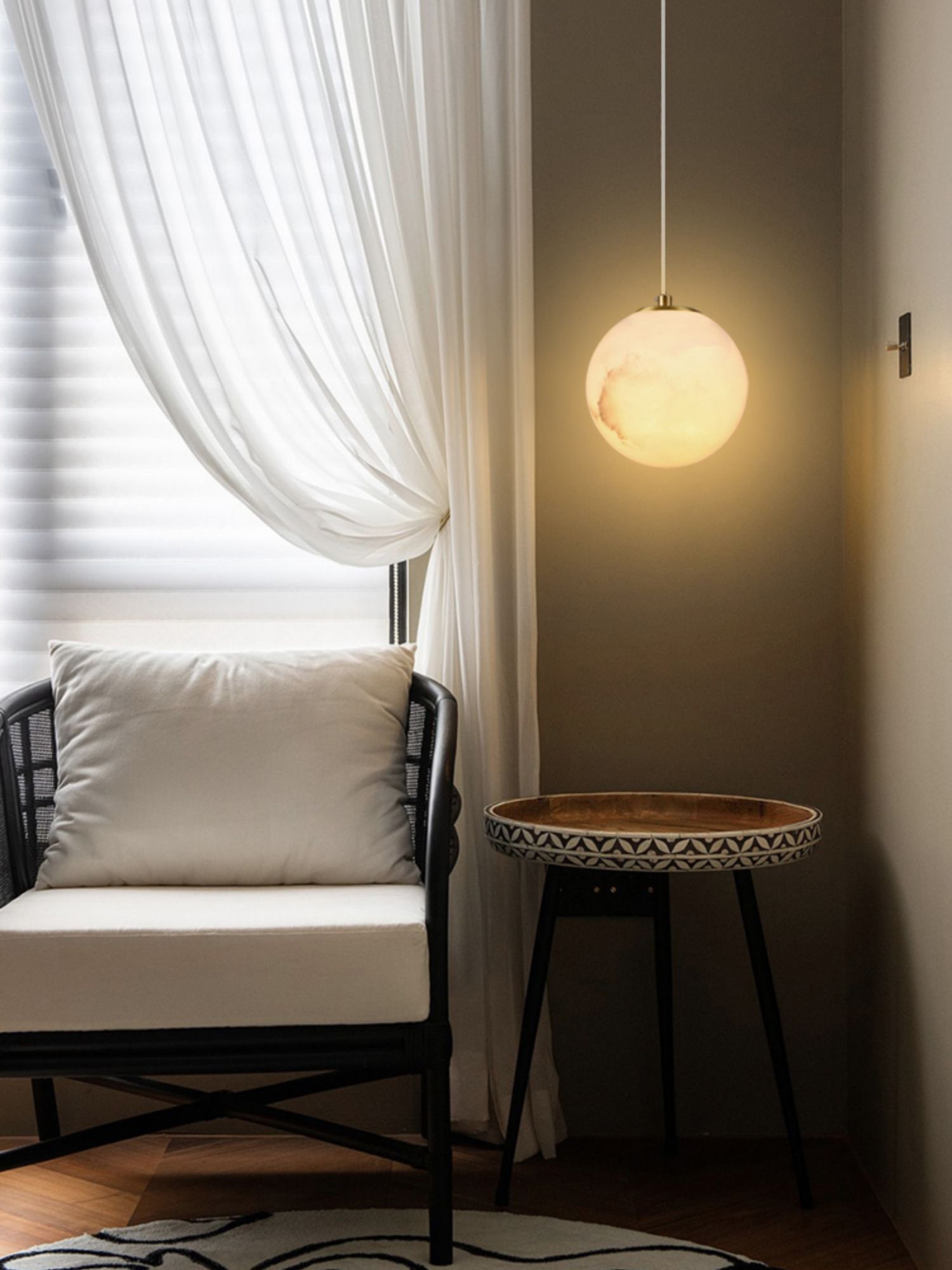 Clérachic Alabaster Globe Pendant Light on a white cord over a round side table, lighting a rattan reading chair by the window.