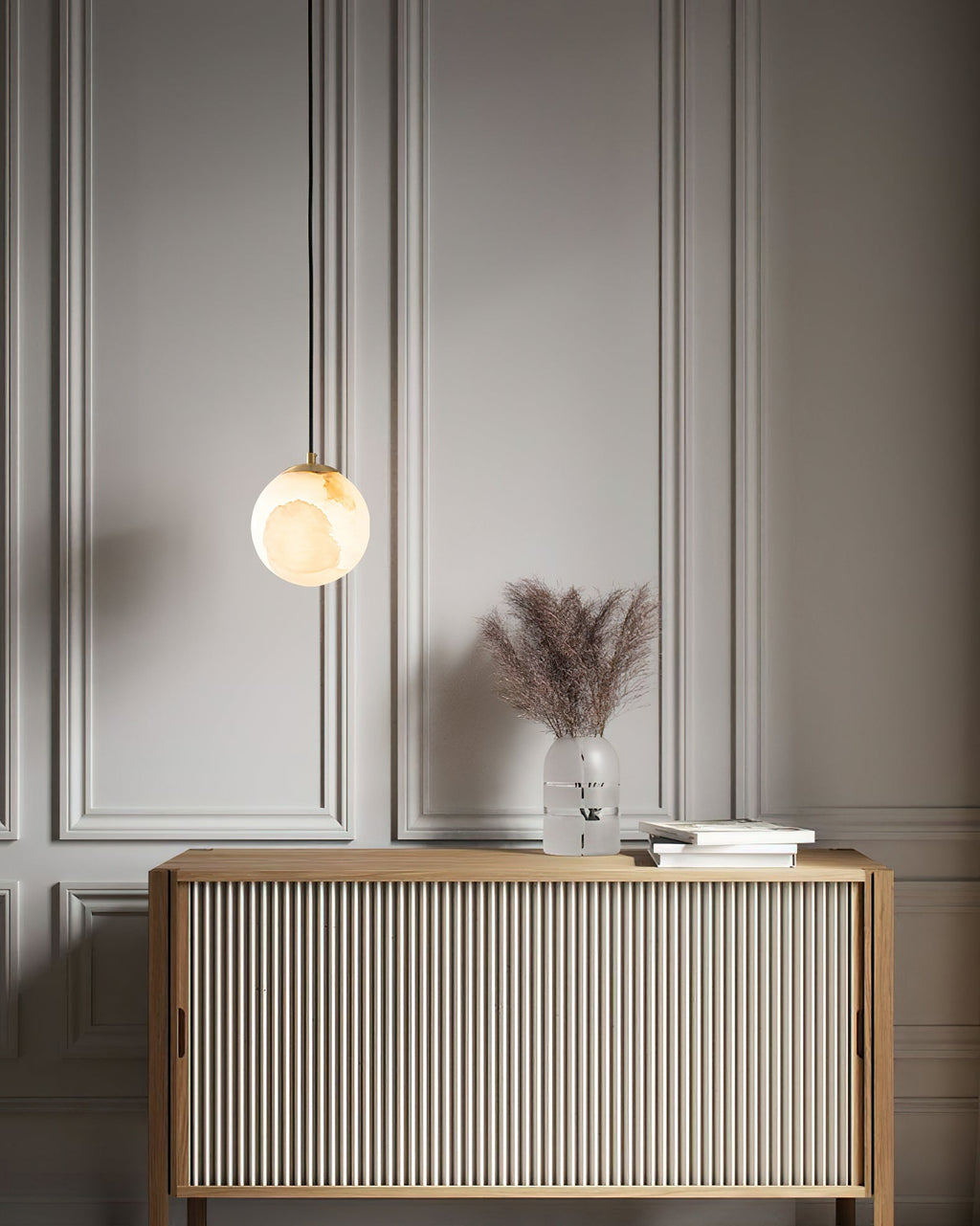 Clérachic Alabaster Globe Pendant Light hung low beside a fluted oak sideboard, warming a panelled hallway wall with dried grasses.