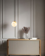 Clérachic Alabaster Globe Pendant Light hung low beside a fluted oak sideboard, warming a panelled hallway wall with dried grasses.