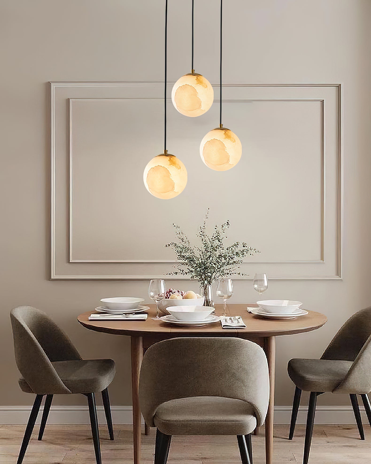 Three globes of the Clérachic Alabaster Globe Pendant Light staggered above a laid dining table, each stone glowing over the plates.