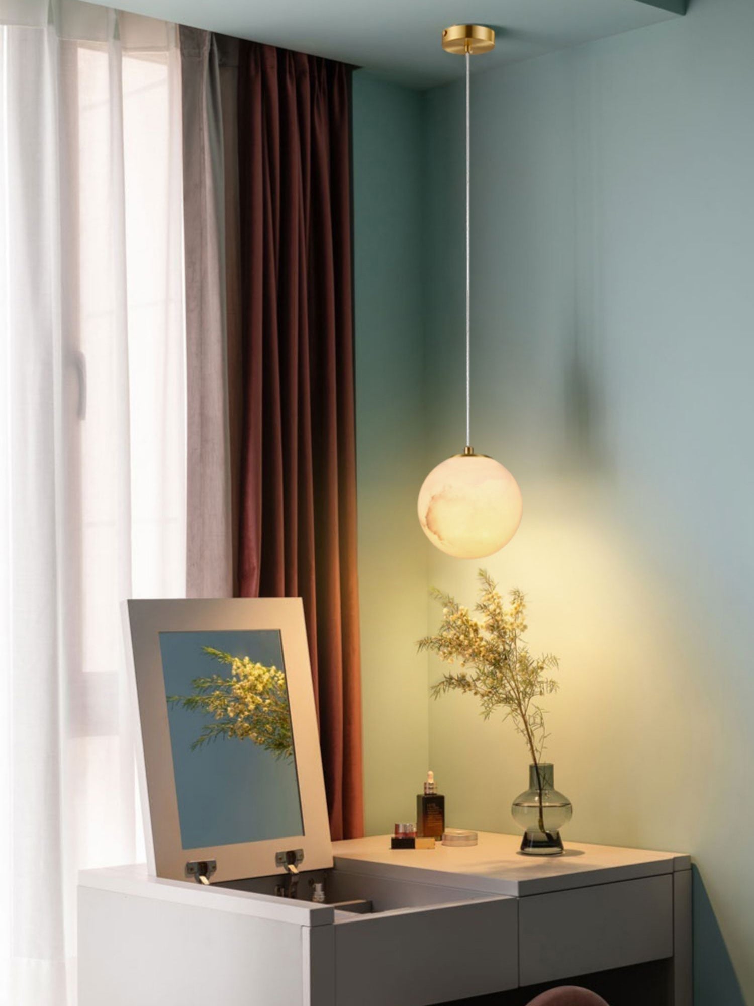 Clérachic Alabaster Globe Pendant Light dropping from a brass ceiling canopy over a dressing table, warm against a soft teal wall.