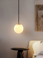 Clérachic Alabaster Globe Pendant Light over a black bedside pedestal, its glow washing a greige wall beside a woven hanging.
