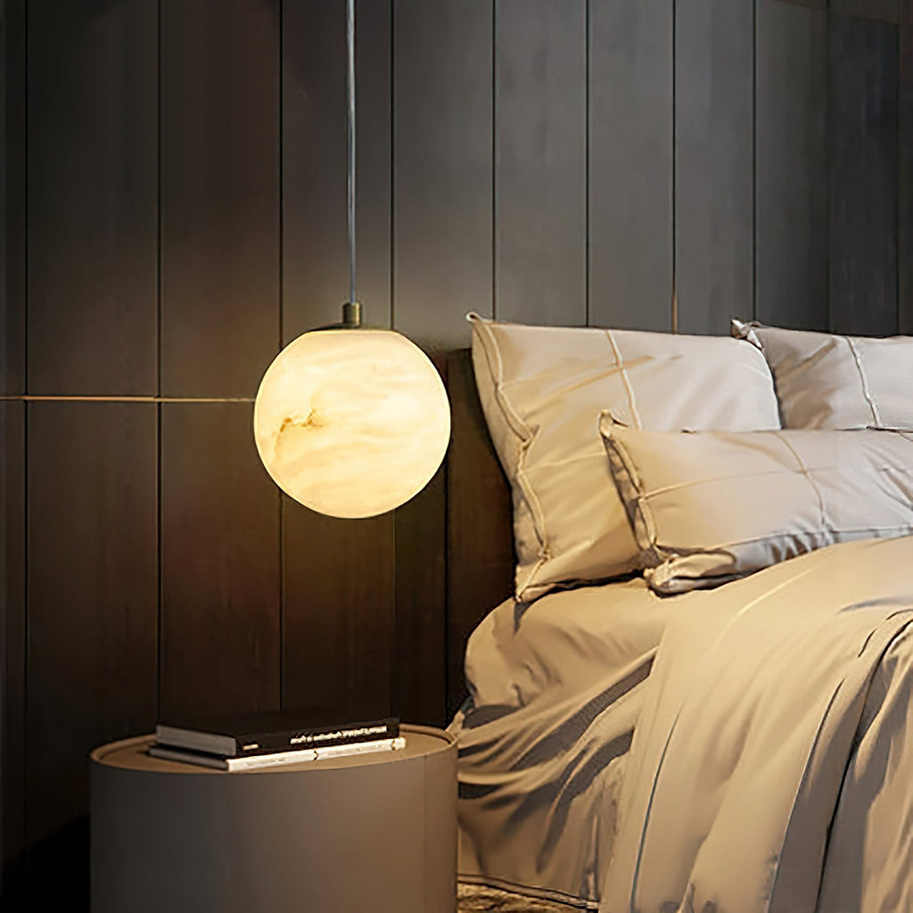Clérachic Alabaster Globe Pendant Light glowing beside a dark timber headboard, throwing warm light across beige bedlinen.